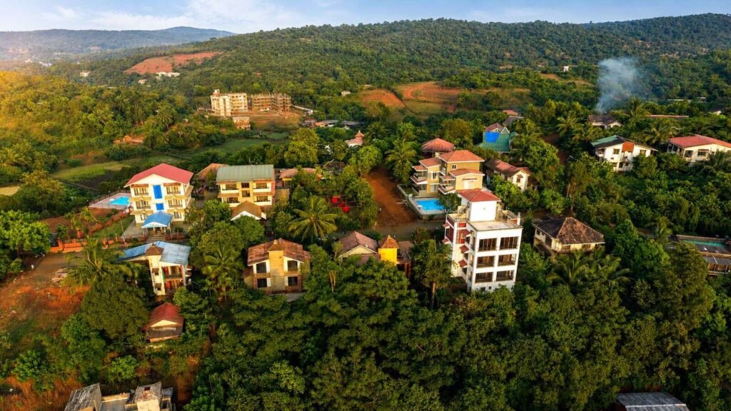 Aerial view of The Mango Inn's villas and holiday homes among coconut palms on a forested Konkan hillside in Dapoli